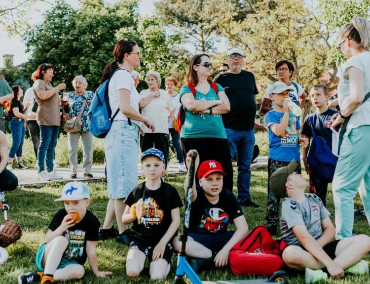 A diverse group of families and children enjoying an outdoor event on a sunny day in a park setting.