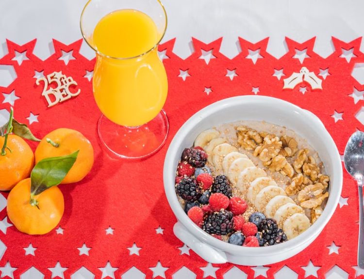 A vibrant breakfast setup with fruits, nuts, and juice on a Christmas-themed mat.