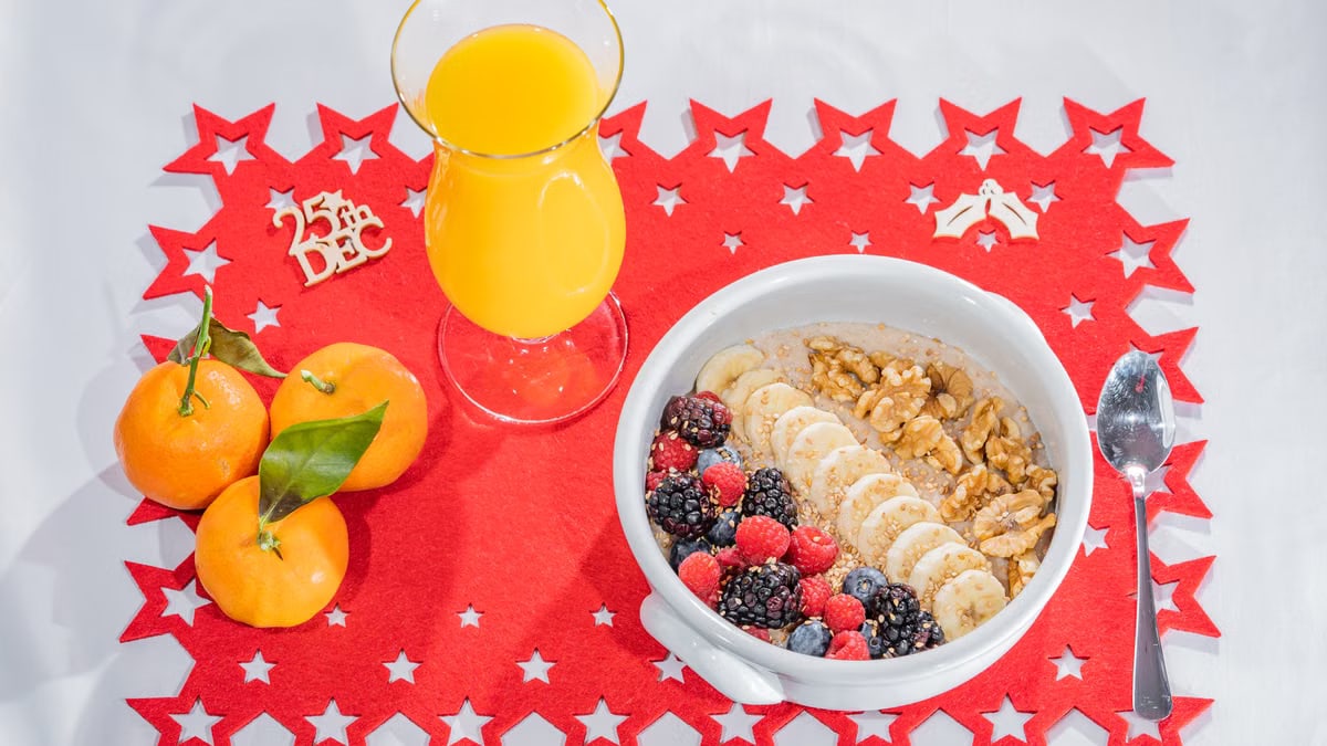 A vibrant breakfast setup with fruits, nuts, and juice on a Christmas-themed mat.
